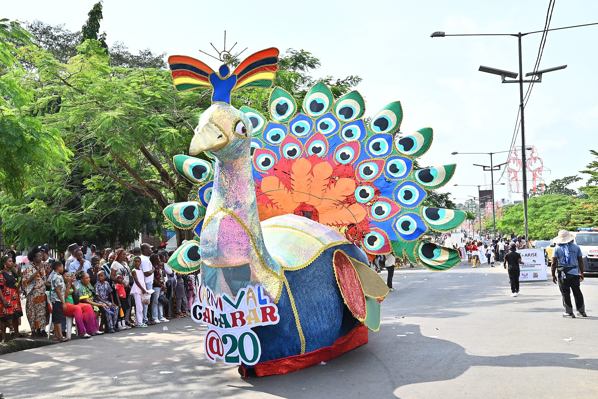 A giant peacock float carrying Carnival Calabar @20 branding moves along a Calabar street as spectators line the roadside during the Calabar Carnival in Cross River State, Nigeria